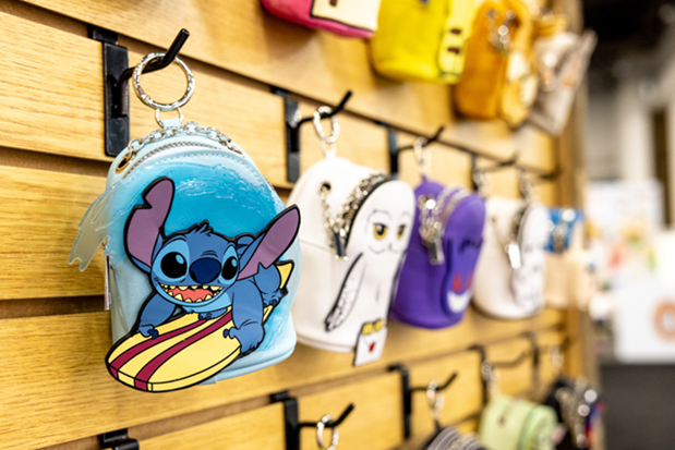 A retail display of licensed mini backpack keychains on a wooden slatwall, showcasing popular characters like Disney’s Stitch and Harry Potter’s Hedwig.
